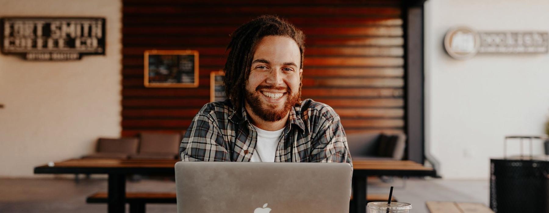 man sits with a drink in front of an open laptop in local restaurant