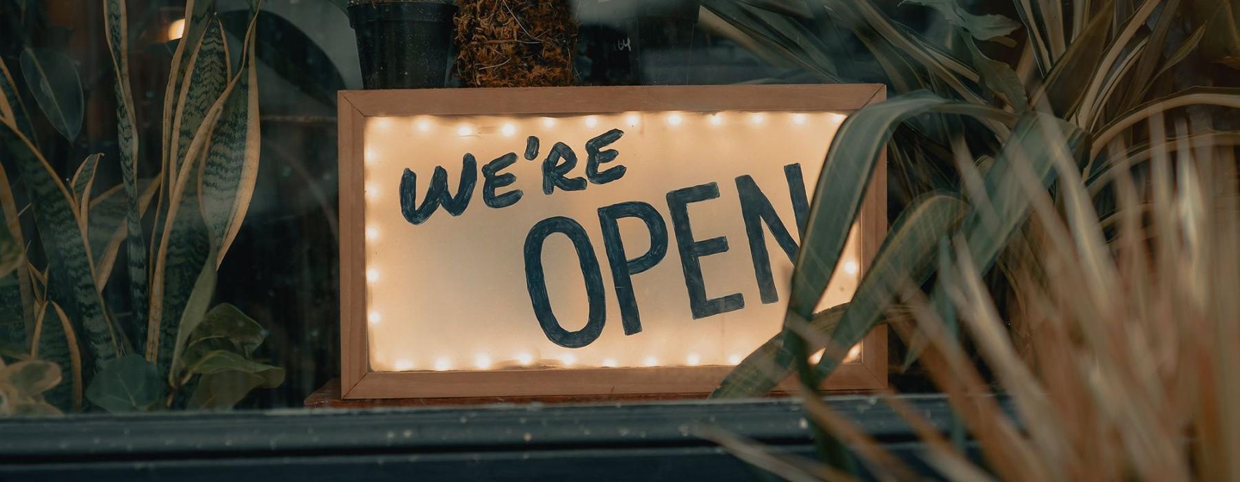 We're Open sign on a window ledge, surrounded by plants